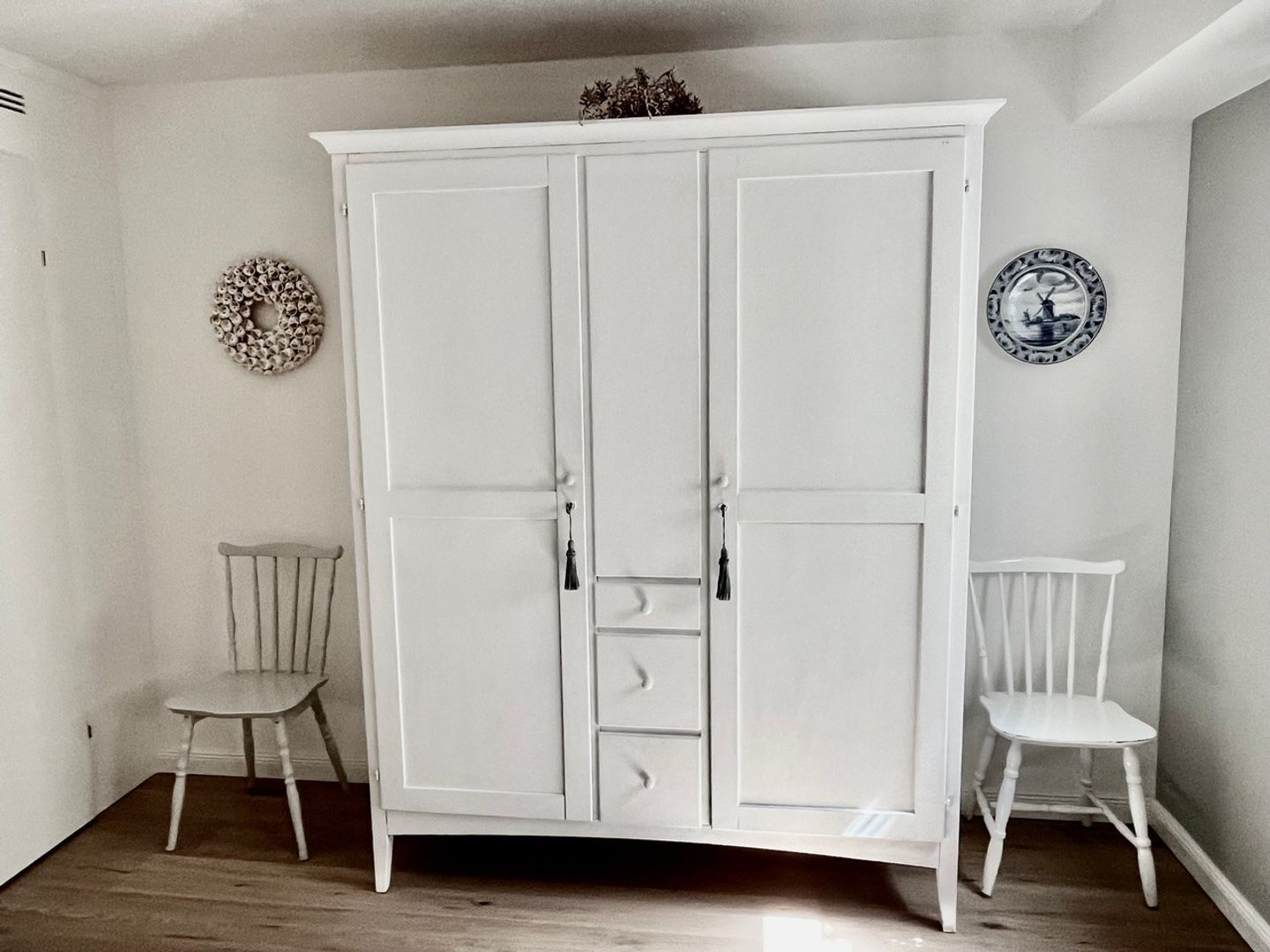 A white wardrobe with multiple doors and drawers, two white chairs, and a wall decoration.