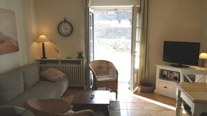 Una sala de estar con un sofá, dos sillones de mimbre, una mesita de centro, un televisor y un reloj en la pared.