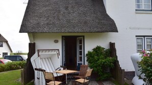 Una casa blanca con techo de paja, un patio con mesa y sillas, y un pequeño jardín.