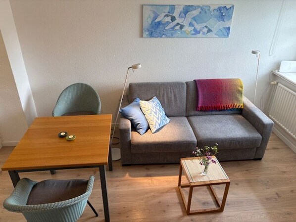 Ein Wohnzimmer mit grauem Sofa, einem Holztisch, einem Korbstuhl und einer Stehlampe.