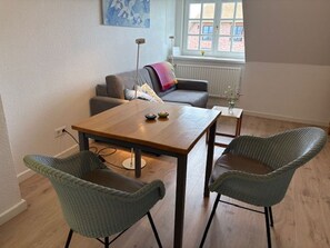 Ein Wohnzimmer mit einem Holztisch, zwei grünen Stühlen, einem grauen Sofa und einer Stehlampe.