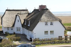 Une maison blanche avec un toit de chaume et un mur de pierre à l’avant.