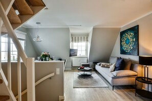 En moderne stue med sofa, sofabord og kunst. En trappe fører til et øvre plan.