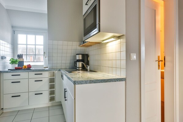 A compact kitchen with white cabinets, a built-in microwave, and a coffee maker. - House Heefkant App. 08 - Heefkant (Sylt)