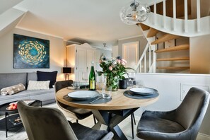 A modern dining area with a round table set for two, a staircase, and a sofa in the background. - House Heefkant App. 08 - Heefkant (Sylt)