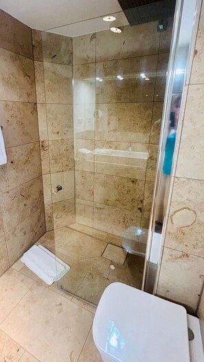 A glass-enclosed shower stall with a white towel on the floor, a white sink, and a tiled wall. - House Heefkant App. 04 - Heefkant (Sylt)