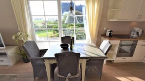 A dining area with a table and chairs, a window with curtains, a coffee machine, and a kitchen area with cabinets and appliances.