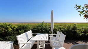 A patio with white furniture, an umbrella, and a view of the sea.