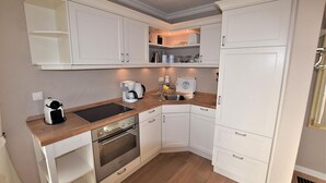 A compact kitchen with white cabinets, a built-in oven, a coffee maker, and a sink.