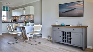 A modern kitchen with white cabinets, a dining table with chairs, a hanging light fixture, and a large painting on the wall.
