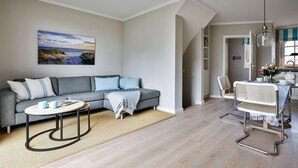 A modern living room with a grey sectional sofa, a round coffee table, and a dining area with a white chair and table.