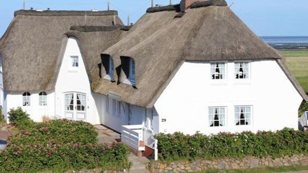 A white house with a thatched roof, a stone pathway, and a view of the sea.