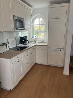 Una cucina con mobili bianchi, un forno a microonde, una macchina del caffè e una finestra con vista.