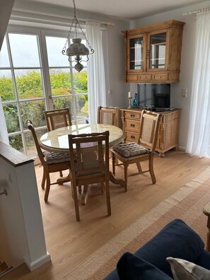 Un coin repas avec une table ronde et des chaises, un meuble en bois abritant un tĂ©lĂ©viseur, et une vue dĂ©gagĂ©e grĂące Ă de grandes fenĂȘtres.