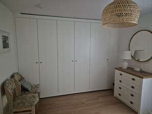 Une chambre comprenant une armoire, une chaise, une commode, un miroir et un luminaire suspendu.