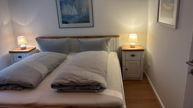 A neatly made bed with two pillows, a bedside table with a lamp, and a framed picture on the wall. - House Heefkant App. 03 - Heefkant (Sylt)