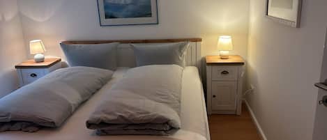 Un lit bien fait, avec deux oreillers, une table de chevet avec une lampe et un tableau encadré au mur.