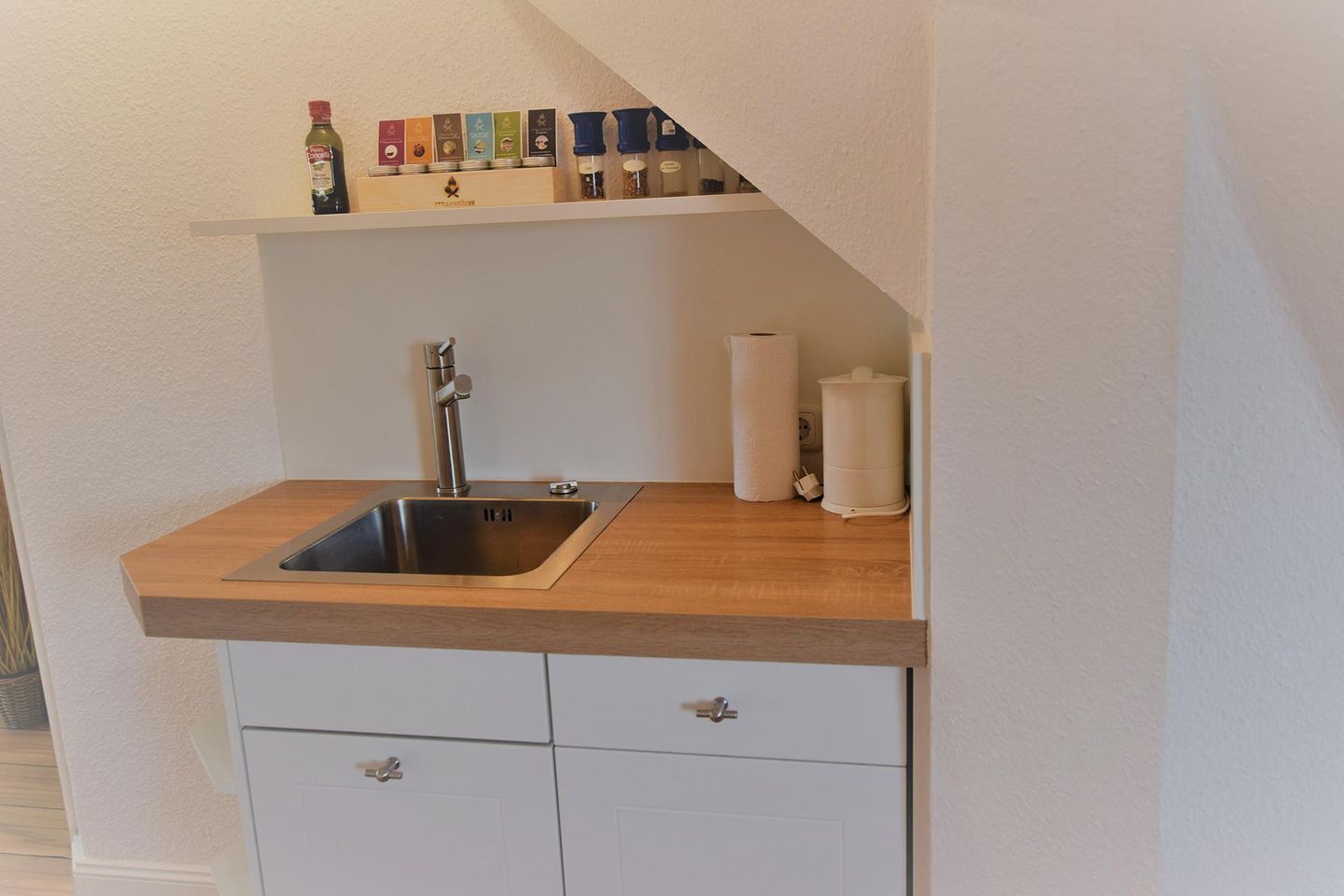 Eine Küche mit Spüle aus Edelstahl, einer Holz Arbeitsplatte und einem Regal mit verschiedenen Gewürzen.