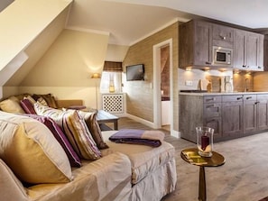 Een gezellige woonkamer met een bank, een glazen tafel met een kaars en een keukenhoek met houten kastjes en een magnetron.