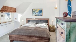 A bedroom with a large bed, a dresser, a wall-mounted lamp, and a surfboard decoration.