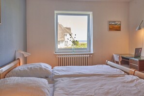 Ein Schlafzimmer mit zwei Betten, einem Fenster mit Blick auf ein GebÀude, einem Schreibtisch mit einem Laptop und einer Heizung.
