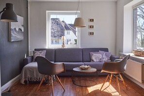 Ein modernes Wohnzimmer mit einem grauen Sofa, zwei schwarzen Sesseln, einem runden Couchtisch und Blick auf einen Berg durch ein Fenster.