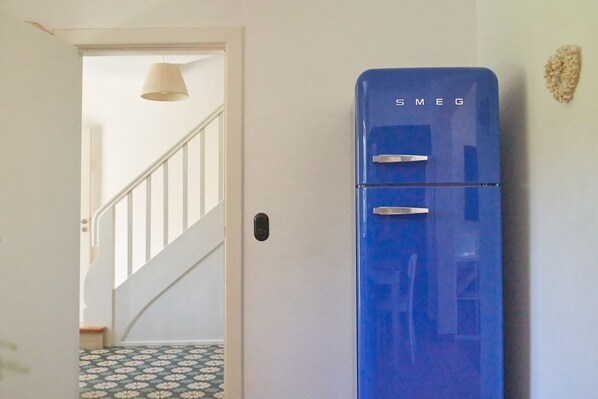 A blue refrigerator with the brand name 'SMEG' in a hallway with a white door, a staircase, and a patterned floor. - Marmelbloom - Marmelbloom MB/01 (Sylt)