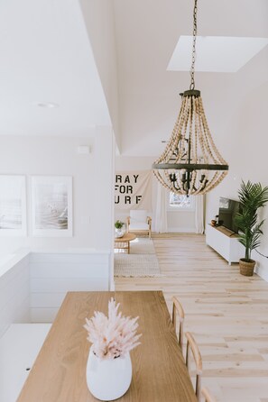 A modern dining area with a wooden table, a white vase with flowers, and a chandelier. - NEW BUILD, Modern coastal home. 10 min walk to beach and sound!  (Kill Devil Hills)