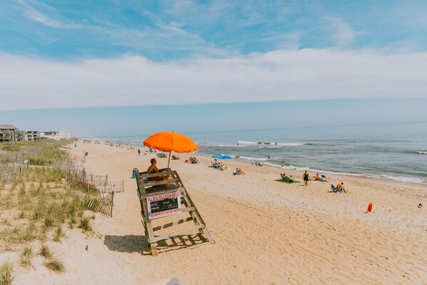 A beach with a lifeguard stand and an orange umbrella. - NEW BUILD, Modern coastal home. 10 min walk to beach and sound!  (Kill Devil Hills)