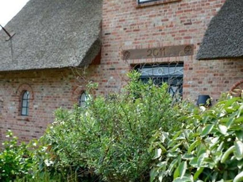 A brick building with a date plaque, a window, and a thatched roof.