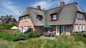 Une maison traditionnelle en briques avec un toit de chaume, un patio doté de meubles d’extérieur et un jardin.