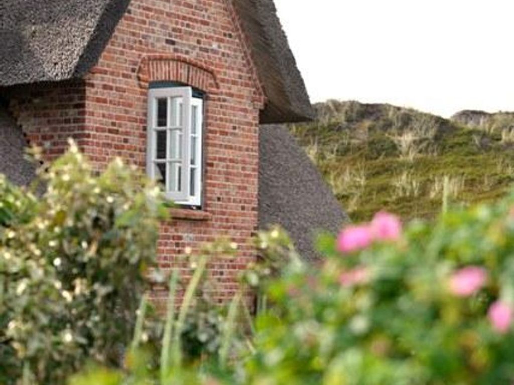 Une maison traditionnelle à toit de chaume, avec une façade en briques et une fenêtre ornée de volets blancs.