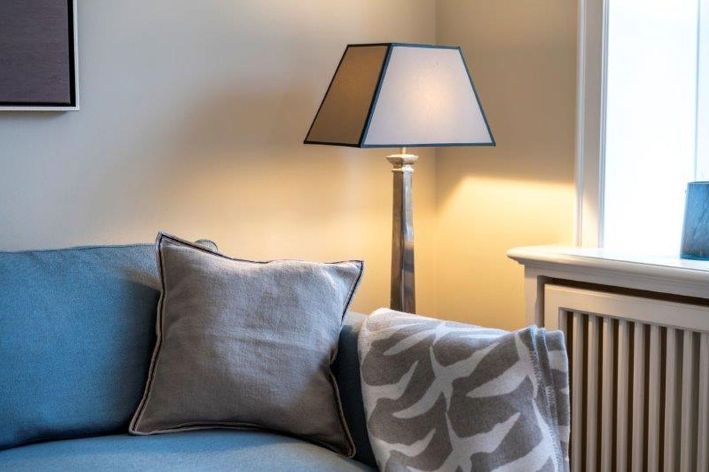 Una habitación con sofá azul, una lámpara de pie y un radiador.