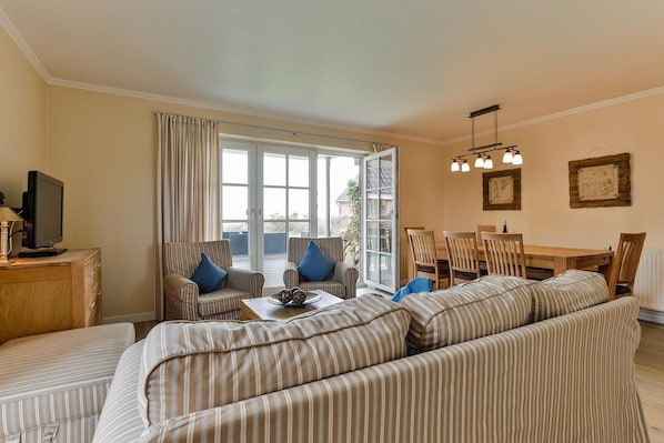 A living room with striped sofas, a television, and a dining area with a table and chairs. - House on the Watt - House on the Watt DO/05b (Sylt)