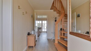 Een hal met een houten trap, een bureau van hout en een grote spiegel.