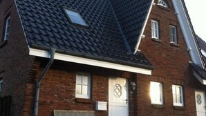 Een woonhuis van baksteen met twee verdiepingen, een flink hellend dak, een klein dakraam en een witte voordeur.