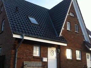 Ein zweigeschossiges Backsteinhaus mit einem steilen Satteldach, einem kleinen Dachfenster und einer weißen Haustür.