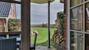 Uitzicht vanuit een kamer met een glazen deur naar een terras. Het terras heeft een stenen muur en een gazon met een metalen stoel.