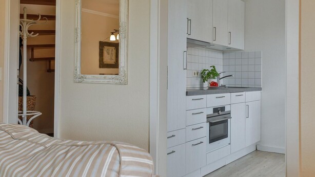 Een kleine keuken met witte kastjes, een inbouwoven en een klein aanrecht.