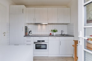 Eine kleine Küche mit weißen Schränken, einem eingebauten Backofen, einer Kaffeemaschine und einem kleinen Topfpflanzen.