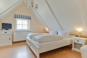 Ein Schlafzimmer mit Bett, Nachttischen, Fernseher, Fenster mit Vorhängen und einer Chandelier.