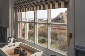 A room with a large window overlooking a coastal landscape, a small sink with a kettle, and a striped valance.