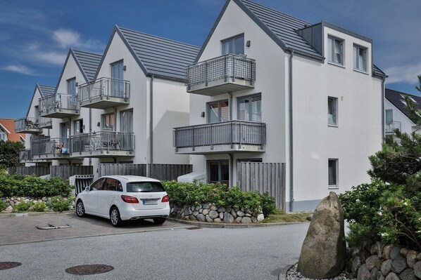 A modern apartment building with balconies, a white facade, and a parked car in front. - Im Dünengrund App. 14 and 15 - Dünengrund (Sylt)