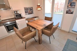 A modern kitchen with a wooden dining table and four leather chairs, a microwave, and a stove. - In the Dünengrund "Dünenrose" - Dünengrund (Sylt)