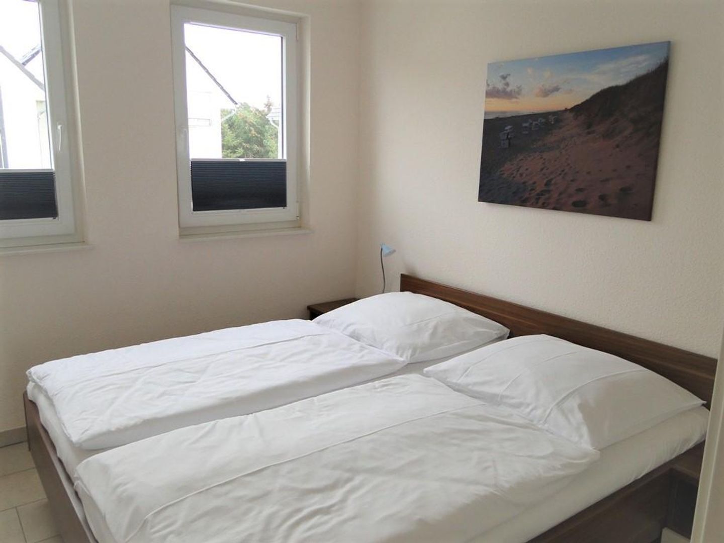 A room with two beds, a window, and a painting on the wall.