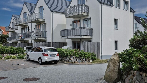 Un edifici modern d'apartaments amb balcons, façana blanca i un cotxe estacionat al davant.