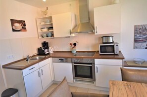 A compact kitchen with white cabinets, a microwave, a coffee maker, and a stove. - In the Dünengrund "Dünenrose" - Dünengrund (Sylt)