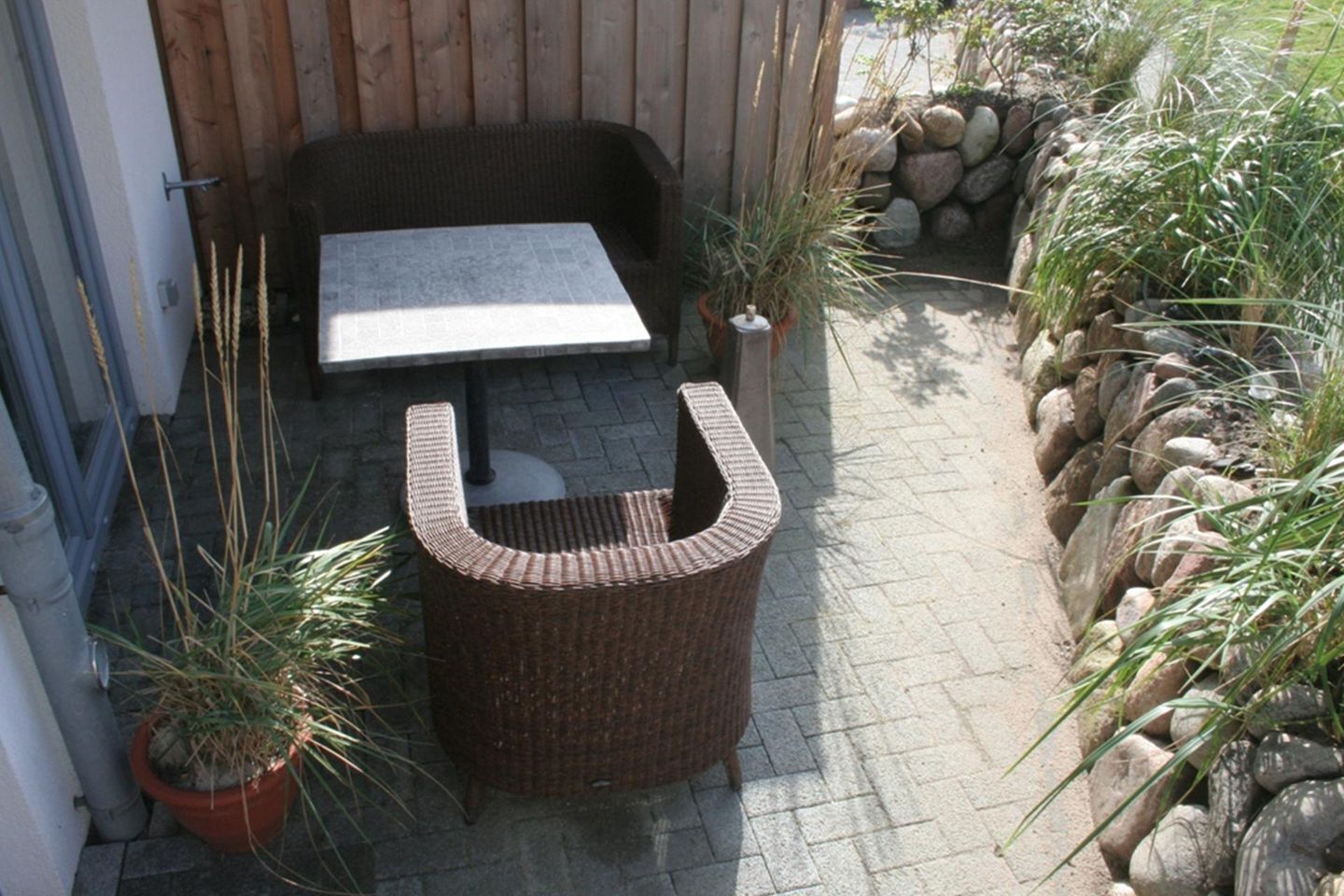 Une chaise en osier, une petite table et des plantes en pot dans un espace patio.