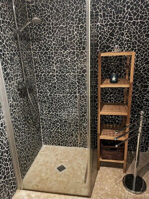 Een douche met een mozaïekwand, een houten plankunit en een metalen vloerlamp.
