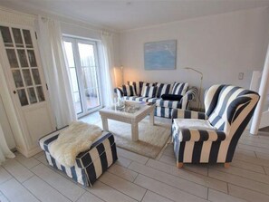 Un salon avec des canapés et des fauteuils à rayures, une table basse et un plaid en fourrure.